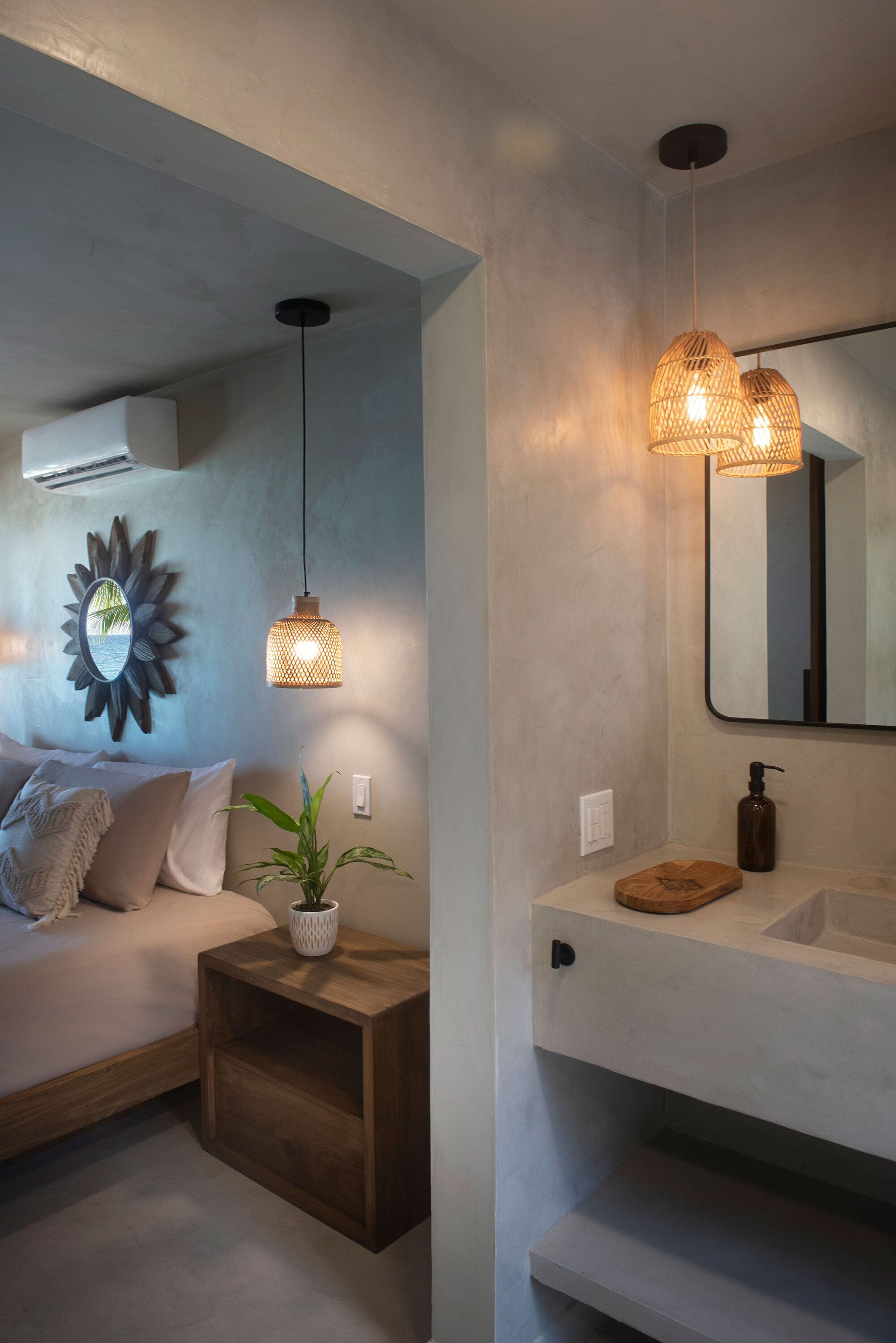 Un baño moderno con un espejo grande, dos lámparas colgantes, una mesita de noche de madera y una planta en maceta.