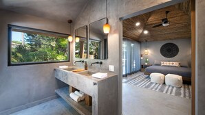 A modern bathroom with a large window, dual sinks, and a ceiling fan. - Arca Boutique Hotel (Roatan)