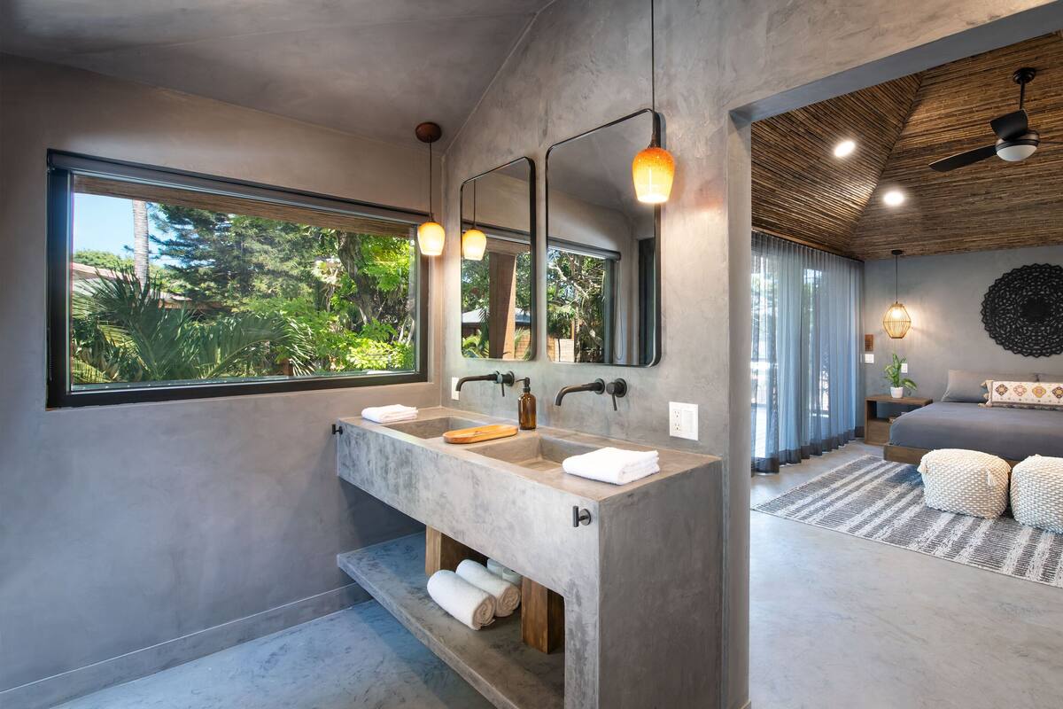 A modern bathroom with a large window, dual sinks, and a ceiling fan.