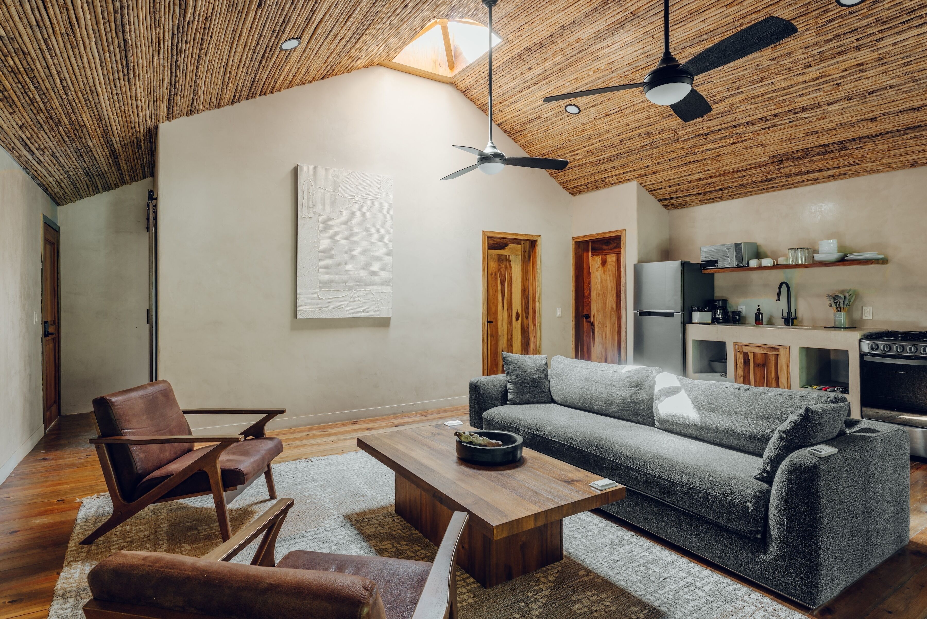 Una sala de estar moderna con techo de madera, un sofá, una mesa de centro y un comedor con refrigerador y electrodomésticos de cocina.