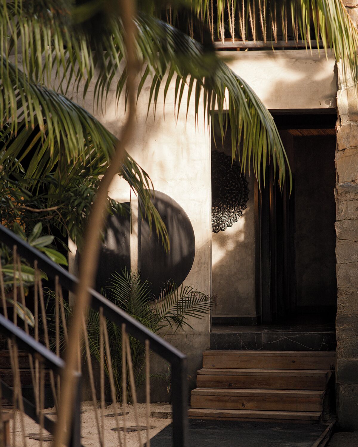 Un edificio moderno con fachada de piedra, una gran maceta circular negra y una escalera de madera que conduce a una entrada oscura.