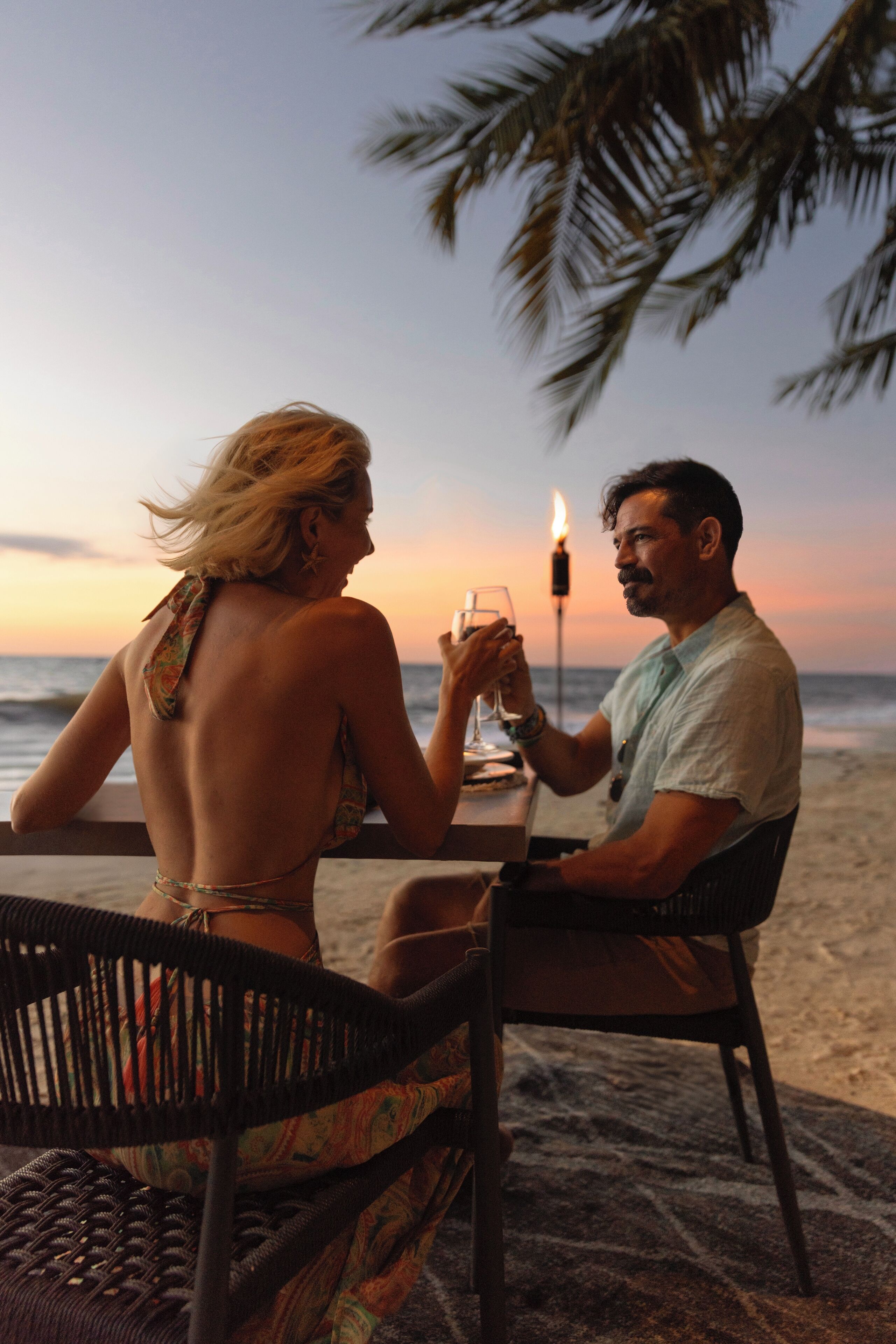 A couple dining at a beachside table with a candle, overlooking the ocean.