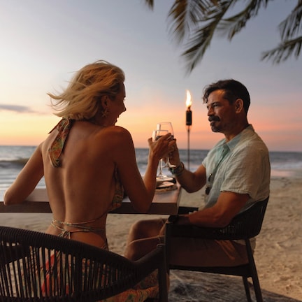 A couple dining at a beachside table with a candle, overlooking the ocean.