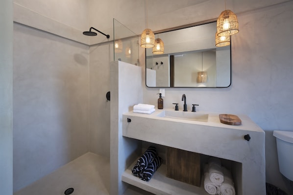 Een moderne badkamer met een glazen douchecabine, een witte wastafel met spiegel en drie hangende rieten lampen.