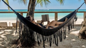 A hammock on a beach with a clear view of the ocean and palm trees. - Arca Boutique Hotel (Roatan)