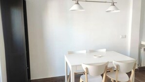 A dining area with a white table and four chairs, a black cabinet, and a hanging light fixture. - Cozy two bedrooms apartment with terrace (Madrid)