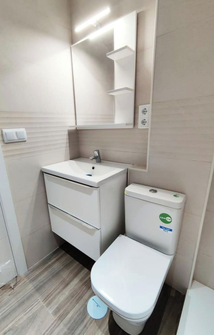 A small, modern bathroom with a white sink, mirror, and toilet.