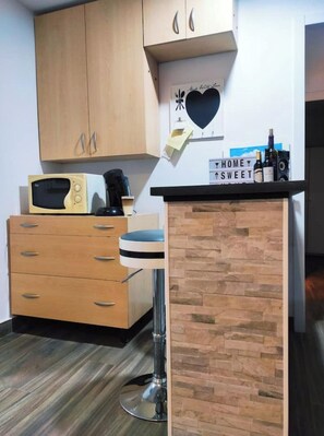 A kitchen with wooden cabinets, a microwave, a coffee maker, and a bar counter with bottles.