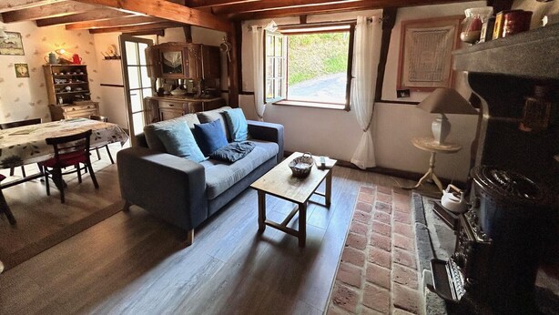 A cozy living room with a sofa, coffee table, and fireplace. There is a dining table with chairs and a kitchen area in the background.