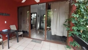 A room with a red wall, a sliding glass door leading to a balcony, a small table with chairs, and a white suitcase on the floor. - Massai Apartments #4 sleeps 5 (Playa Flamingo)
