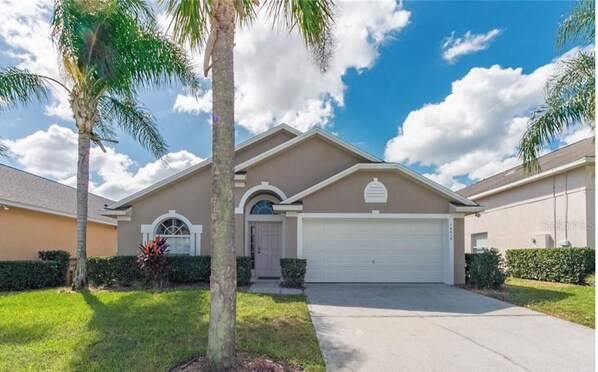 Stunning single-story home with a central entrance, arched windows, and a garage, set amidst lush lawns and mature trees.