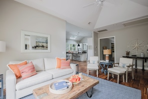 A modern living room with a white sofa, a wooden coffee table, and a dining area with a white chair and a small table.