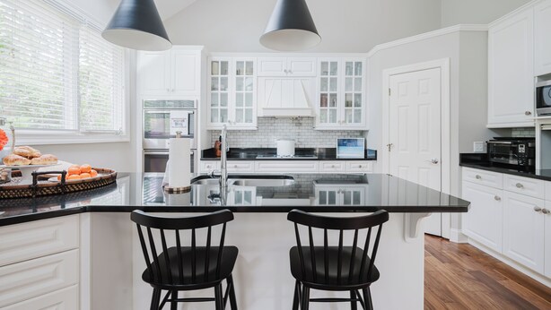 A modern kitchen with white cabinetry, a black countertop, two black bar stools, and pendant lighting. - Beautiful spacious home close to the beach! (Hilton Head Island)