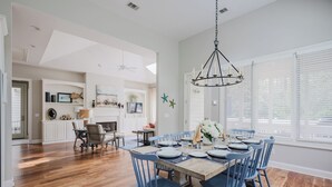 A dining area with a wooden table set for six, blue chairs, and a chandelier. - Beautiful spacious home close to the beach! (Hilton Head Island)