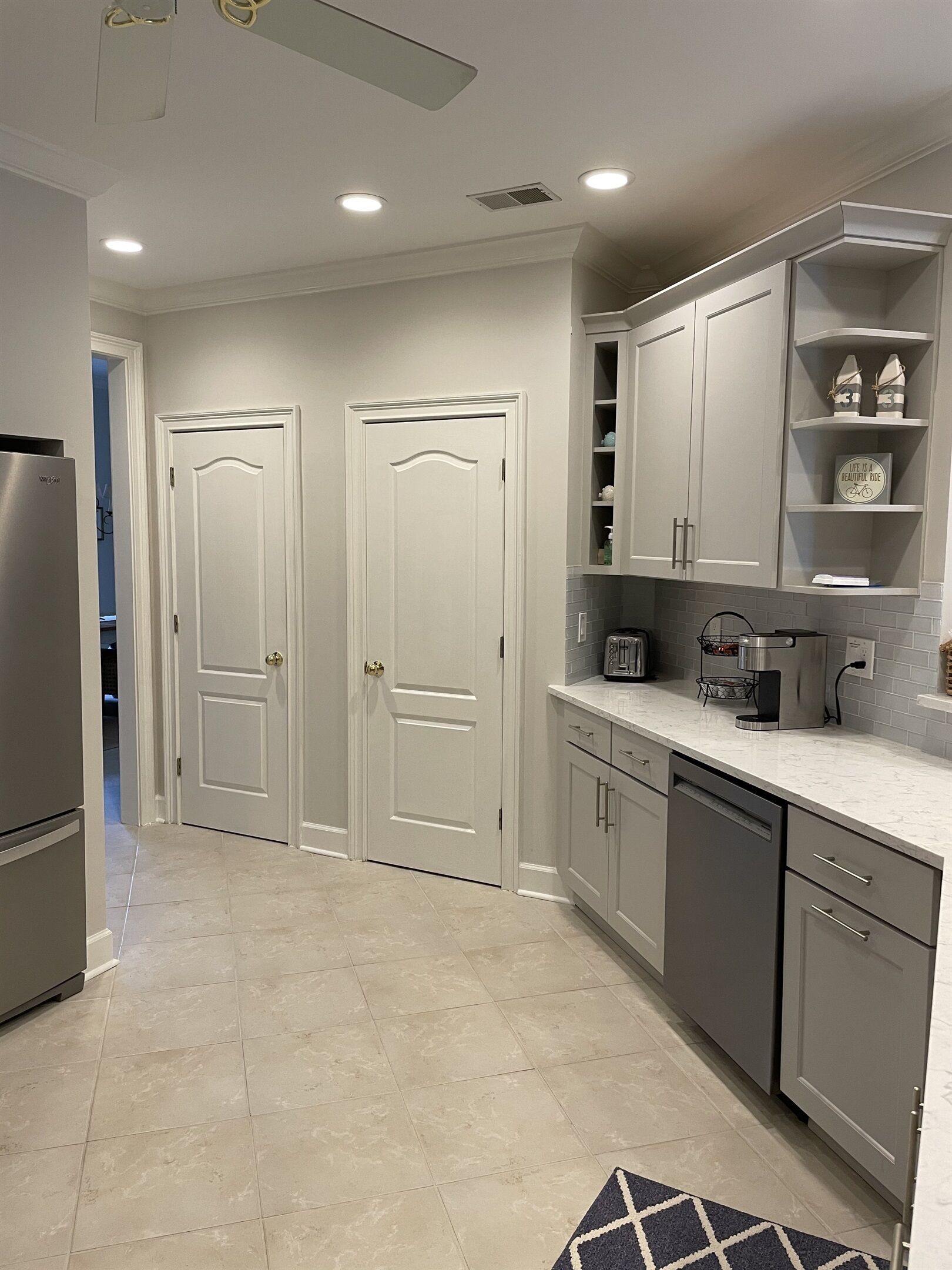 A kitchen with two white doors, a refrigerator, a dishwasher, and a countertop with a coffee maker and toaster.