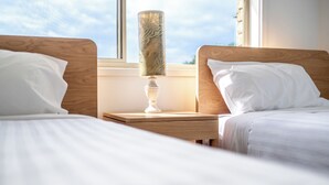 A hotel room with two beds, a nightstand with a lamp, and a window with a view of the sky.