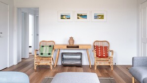 A room with two wicker chairs, a small wooden table, and a radiator. There are three framed pictures on the wall.