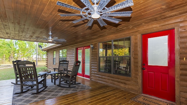 Una cabaña de troncos con terraza de madera, sillas mecedoras y una puerta roja.