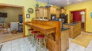 Una cocina con armarios de madera, una isla central con taburetes y un área de comedor con una silla roja.