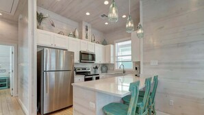 Una cocina moderna con armarios blancos, electrodomésticos de acero inoxidable y sillas color turquesa en la isla.
