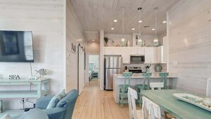 Una cocina moderna con armarios blancos, un refrigerador de acero inoxidable y un comedor con una mesa verde y sillas blancas.