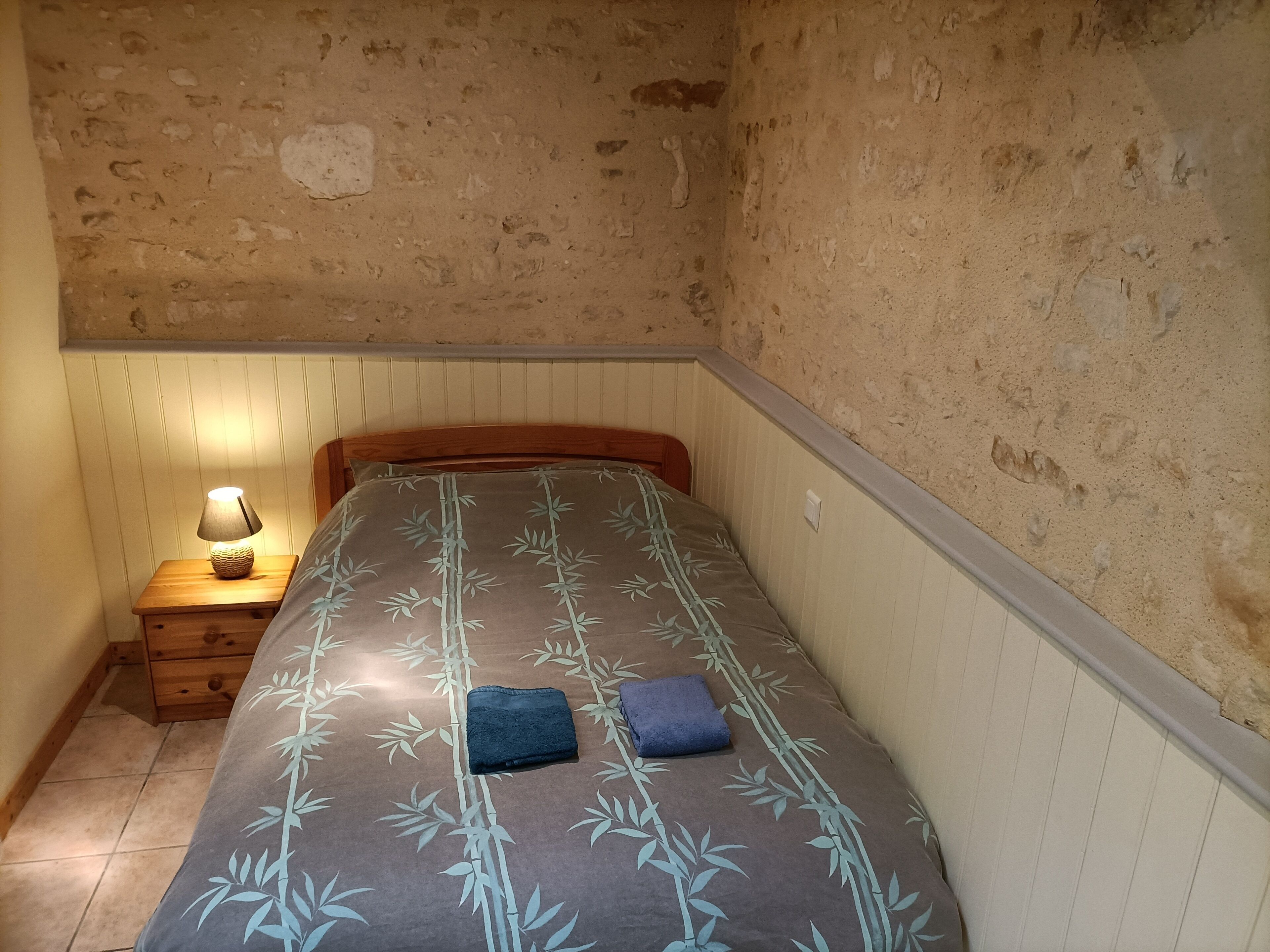 Ein kleiner, rustikaler Raum mit einem Einzelbett, einem Nachttisch mit Lampe und einem Holzkopfteil.