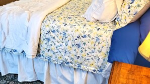 Un dormitori amb un llit, una nitòria de fusta, una catifa amb dibuixos i una porta que dona a una altra habitació.