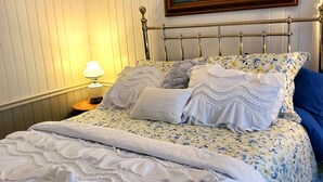 Un llit ben fet amb roba de llit blanca i un edredó amb un disseny floral, un capçal de fusta i un quadre d'una escena de port a sobre.
