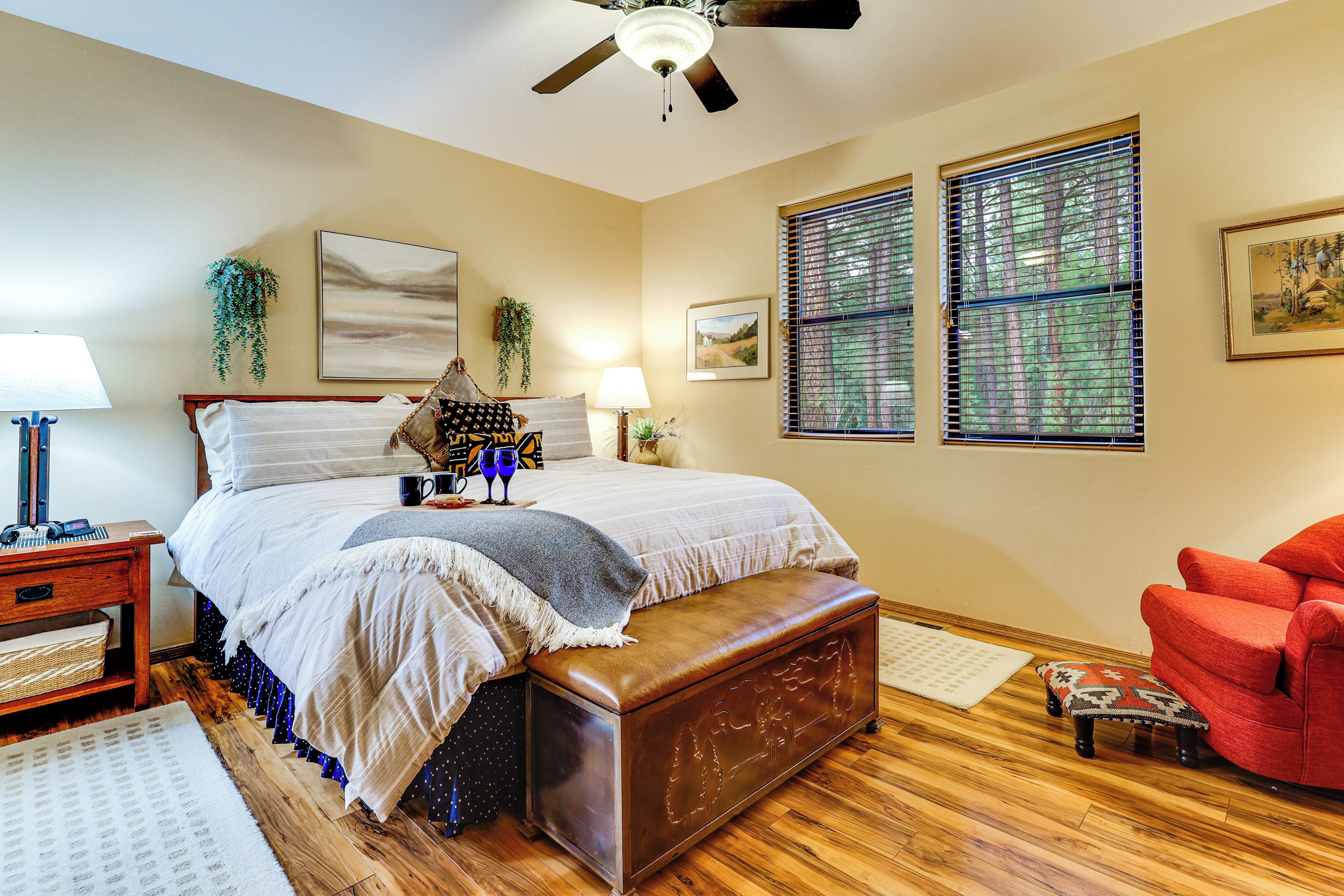 A bedroom with a bed, bedside tables, a red armchair, a ceiling fan, and a window with blinds.