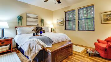 A bedroom with a bed, bedside tables, a red armchair, a ceiling fan, and a window with blinds.