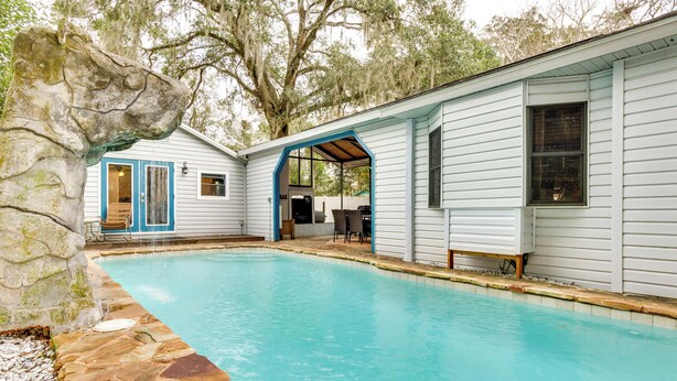 A pool area with a stone border, a covered patio, and a house with blue accents. - Mt Dora Couple's Retreat w/ Shared Pool! (Mt Dora)