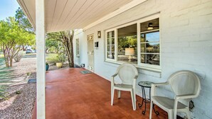 A covered porch with two white chairs and a small table, a white brick wall, and a window overlooking a street. - Centrally Located Tucson Home ~ 5 Mi to Dtwn! (Tucson)