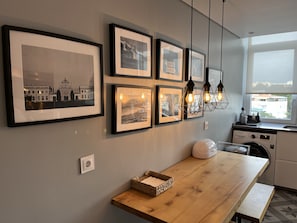 A modern kitchen with a wooden table, framed pictures on the wall, and a view of the city through the window.