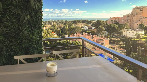 Un balcone con vista su una cittadina costiera, tra edifici e vegetazione.