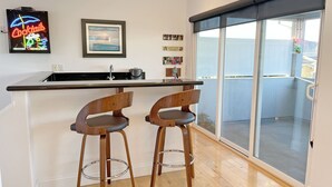 Una cocina moderna con barra, dos taburetes de madera, un letrero de neón y un cuadro en la pared.
