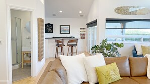 Una sala de estar moderna con un sofá de cuero marrón, un ventanal con vistas y una zona de cocina con taburetes de bar.