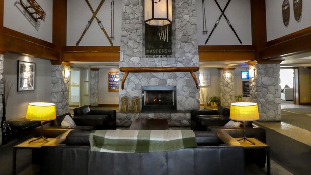 A lobby with a stone fireplace, wooden beams, and a checkered sofa. - Ski-in-Out, 3 Hot Tubs & Pool. Re-done unit, in suite Washer/Dryer, Full Kitchen (Whistler)