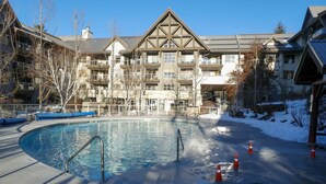 A swimming pool with a pool ladder, surrounded by orange traffic cones, and a building with a traditional architectural style in the background. - Ski-in-Out, 3 Hot Tubs & Pool. Re-done unit, in suite Washer/Dryer, Full Kitchen (Whistler)