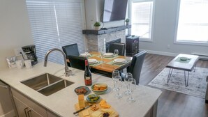 A modern kitchen with a large island, a dining area, and a living space. - Ski-in-Out, 3 Hot Tubs & Pool. Re-done unit, in suite Washer/Dryer, Full Kitchen (Whistler)