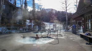 A hot spring area with a pool, benches, and a stone wall. - Ski-in-Out, 3 Hot Tubs & Pool. Re-done unit, in suite Washer/Dryer, Full Kitchen (Whistler)