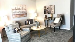 A living room with a sofa, armchair, coffee table, and a side table with decorative items. - Perfect Oasis. NEW Home Away from Home with COVERED PARKING-Close to everything (Stillwater)