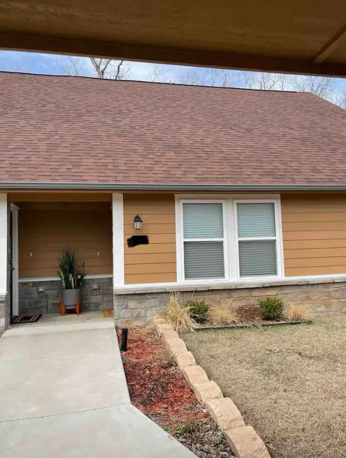 A residential house with a brick roof, a front porch, and a small garden area with mulch and plants.