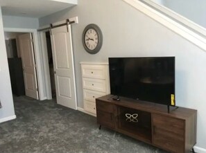 A hallway with a sliding door, a clock, a TV on a wooden cabinet, and a coat rack.