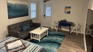 Ein Wohnzimmer mit Sofa, Couchtisch, einem kleinen Tisch mit Stühlen, einem Gemälde und einem Deckenventilator.