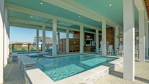 Une piscine à l’eau cristalline, entourée de piliers blancs et surmontée d’un plafond turquoise.