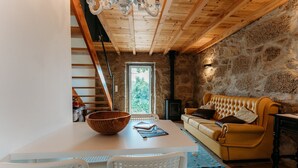 A cozy room with a stone wall, a wooden ceiling, a yellow sofa, a white table with a wooden bowl, and a fireplace.