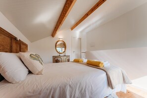 A bedroom with a wooden ceiling, a bed with white bedding, a dresser with a mirror, and a window with natural light.