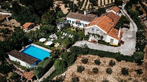 Vue aérienne d’une propriété comprenant une piscine, une maison en pierre et un jardin avec un espace salon extérieur.