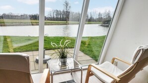 Un balcon donnant sur un lac, une petite table avec une plante et deux chaises.