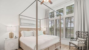 Een hemelbed met houten frame, een nachtkastje met een geweven lamp en een stoel met een geweven rugleuning.